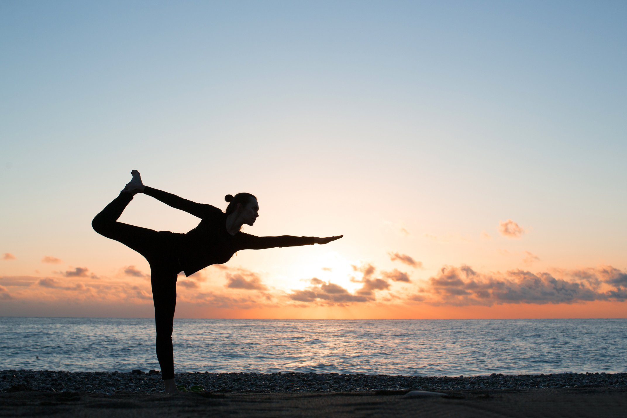 silhouette of woman practicing yoga on the beach at sunset